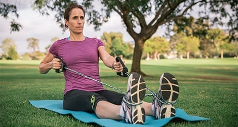 Woman seated on ground with resistance band around feet