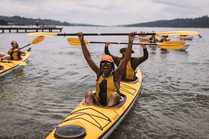 A group of kayakers on a lake raising their paddles and having fun