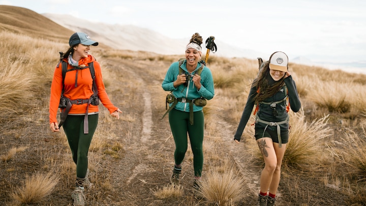 Three hikers laugh while hiking a grassy trail on New Zealand's south island.