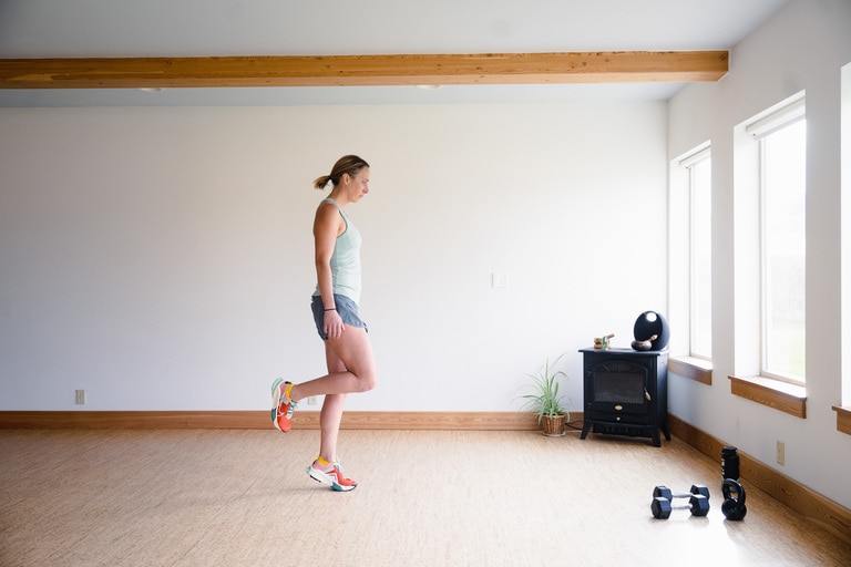 A woman performs a single-leg calf raise while holding a kettlebell