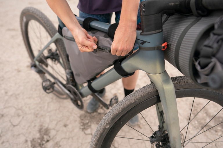 A cyclist zips up a frame pack on a gravel bike.