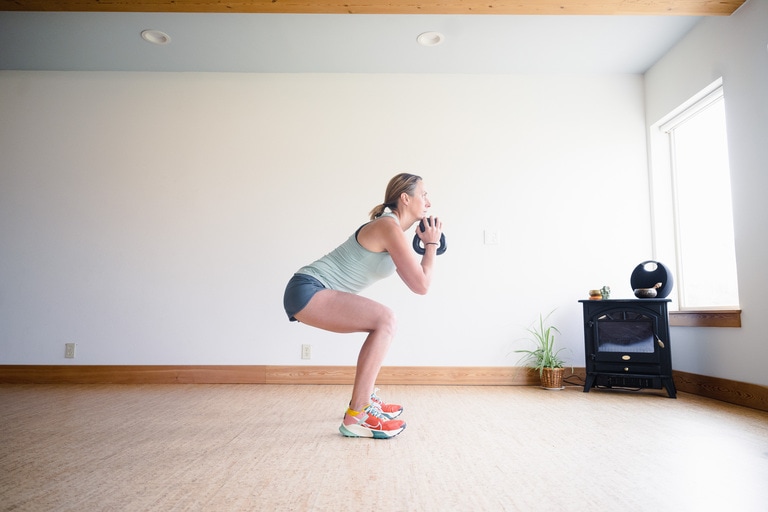 A woman squats while holding a kettlebell