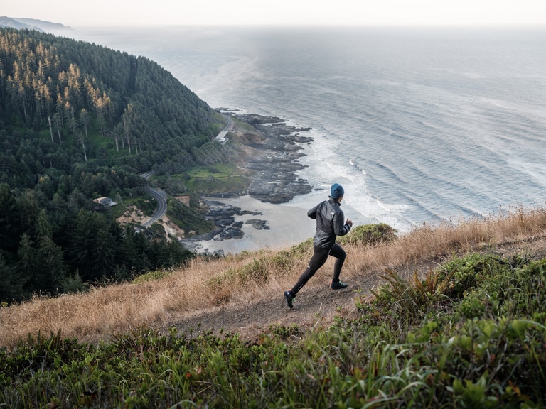 A person running up a hill on a bluff trail with the ocean in the background