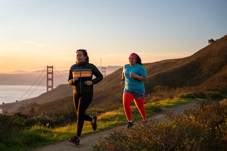 Two women run on a trail near the Golden Gate Bridge