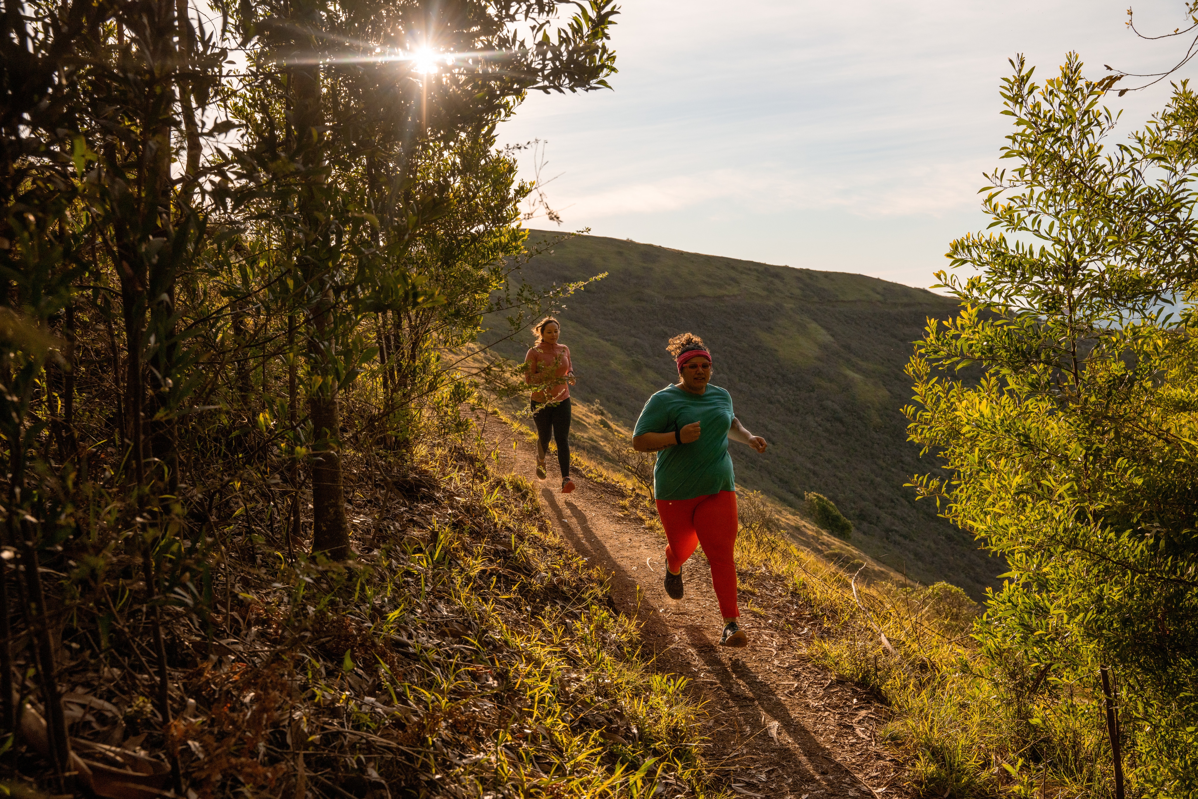 Two people running up an winding trail in the woods.