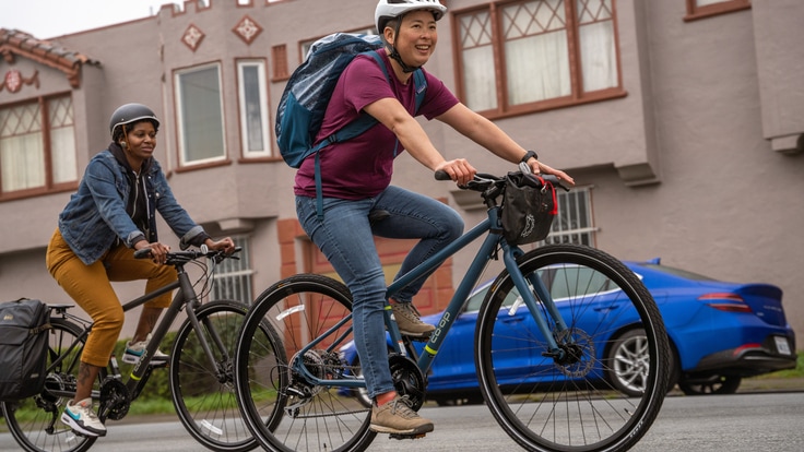 Two people riding bikes along in an urban neighborhood