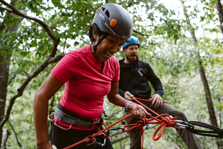 A person is smiling and preparing to rope climb while another looks on