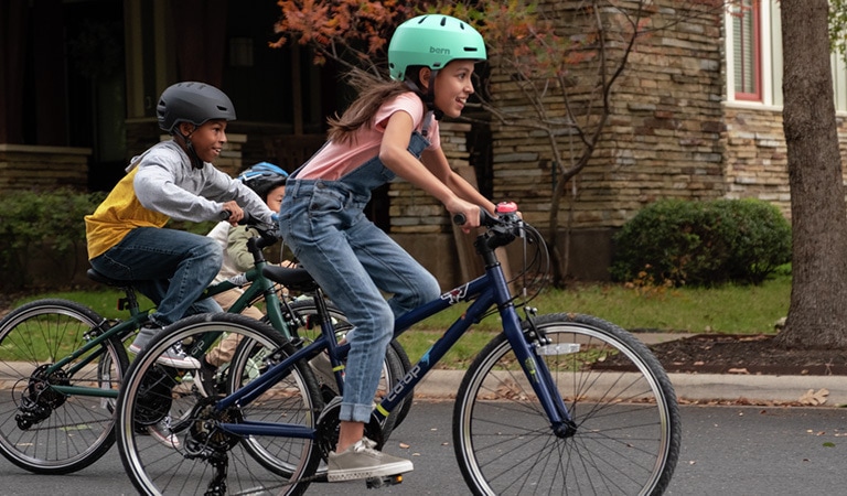 Two kids wearing helmets are riding though the neighborhood on their new bikes.