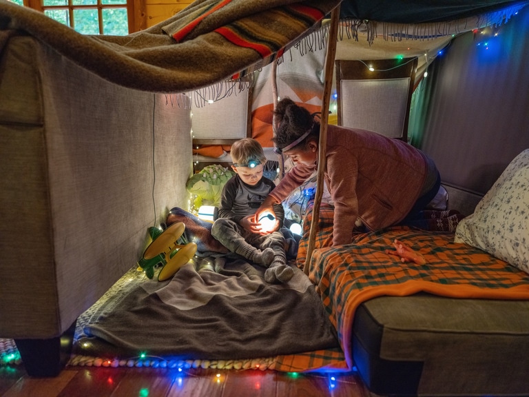 Young girl helps a young boy turn on a light in his at-home tent.