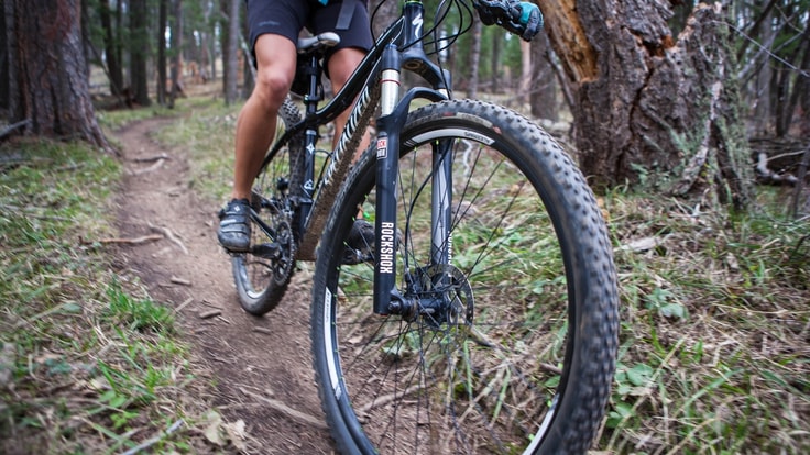 Photo of the bottom half of a mountain bike on a wooded trail.