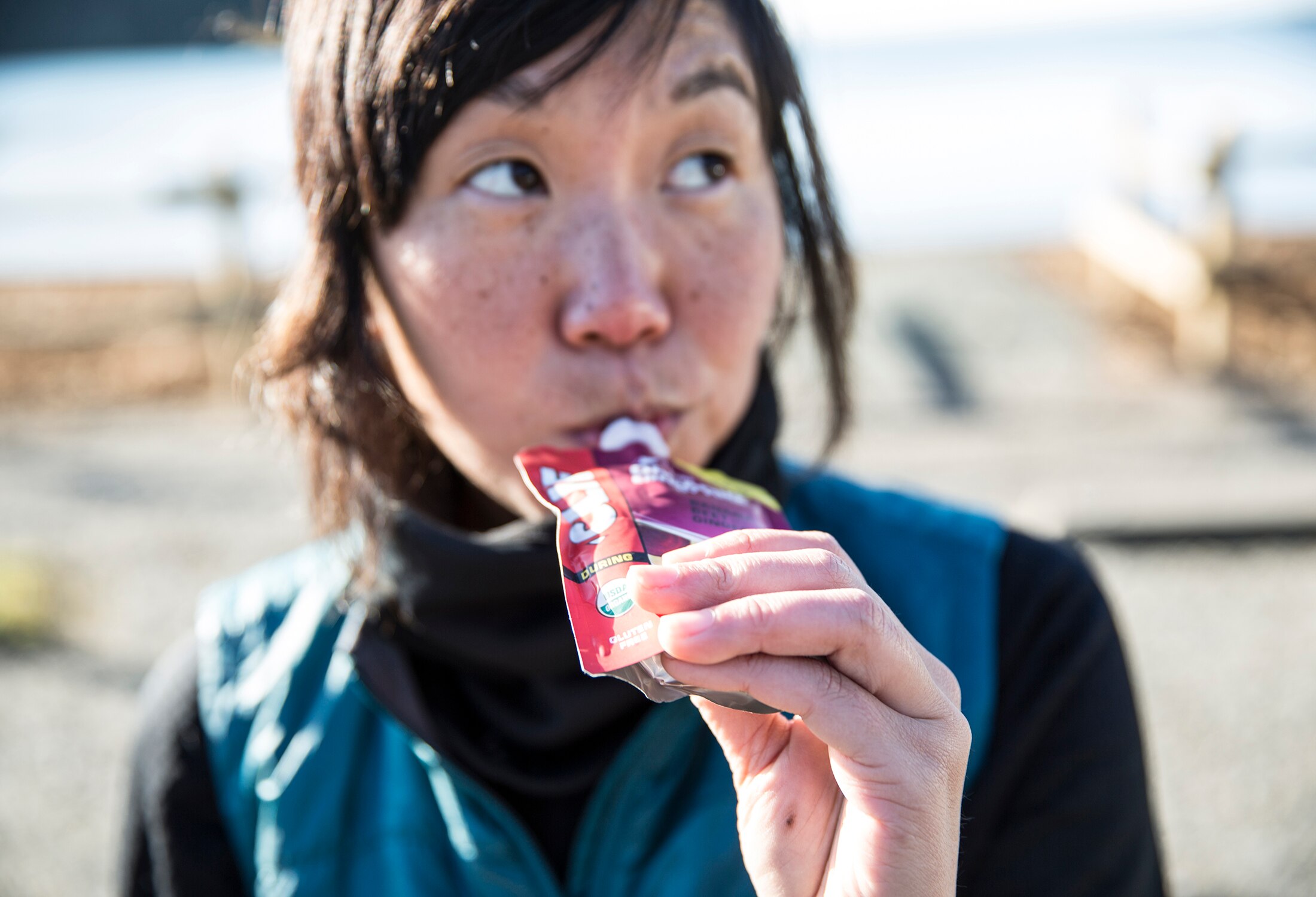 A person in a blue vest eats a Clif gu packet.