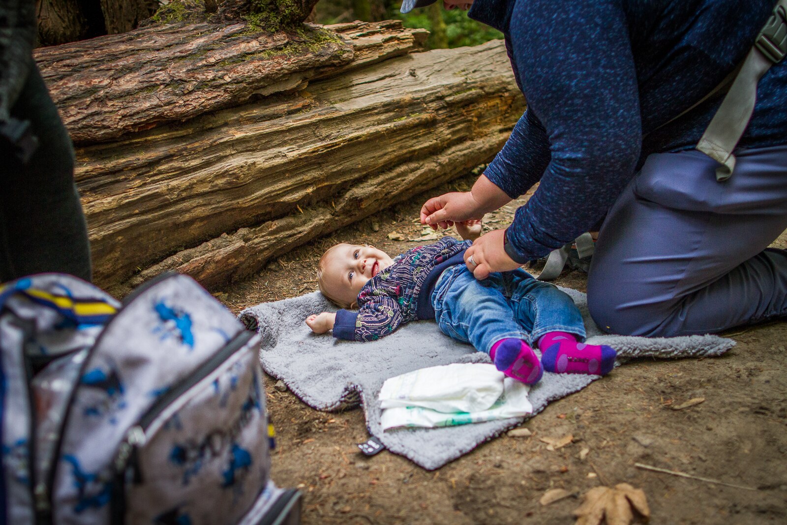 A smiling toddler gets their diaper changed on the trail