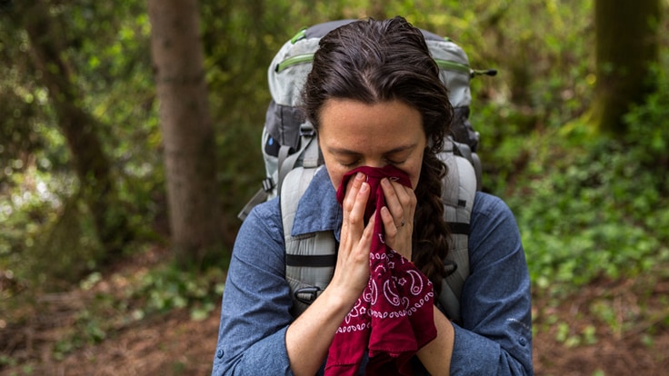 an ill backpacker holding a bandana to their face