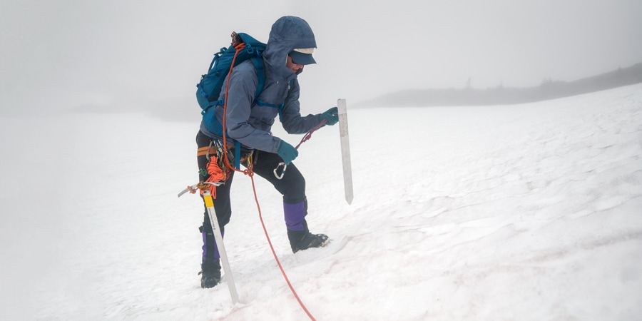 The lead climber on a roped team attaches her rope to a snow picket