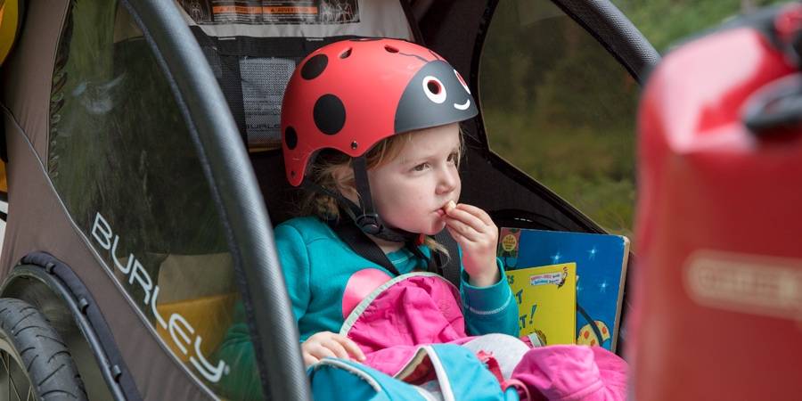 A little girl eating snacks while sitting in a bike trailer