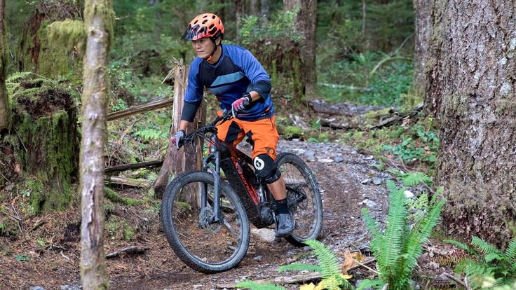 A mountain biker riding an electric mountain bike on a trail in a mossy forest