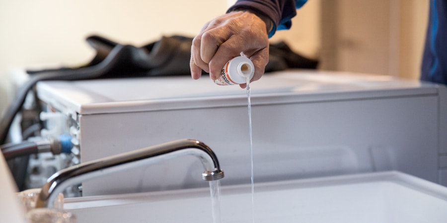 Pouring wetsuit cleaner into a tub of water