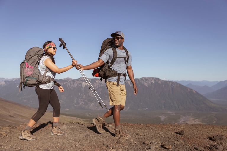 Two hikers along a ridge pass a pair of hiking poles to each other